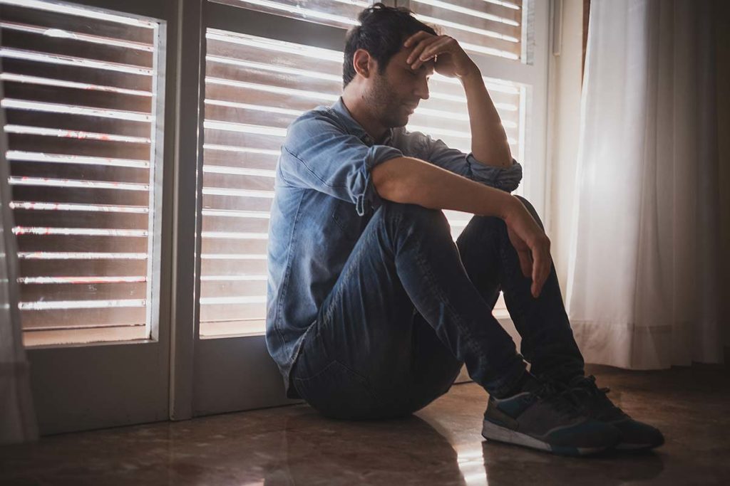 Man sitting near shuttered window, wondering, "How long does opiate detox take?"
